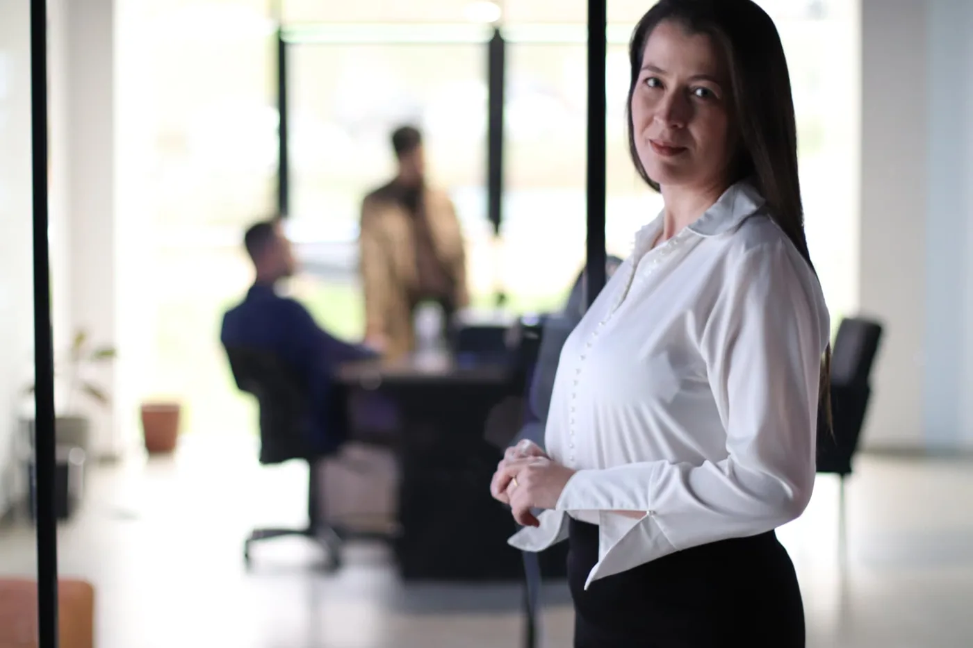 Mulher em escritório contemporâneo com equipe em conversa ao fundo